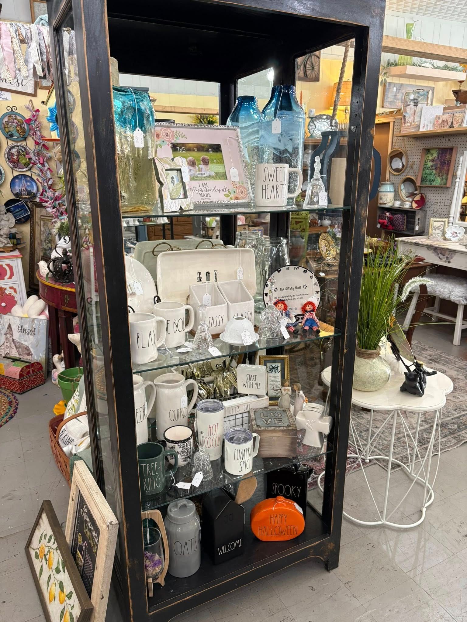 Shelved display of ceramic decor and framed art in a shop, with colorful glass items and trinkets around it
