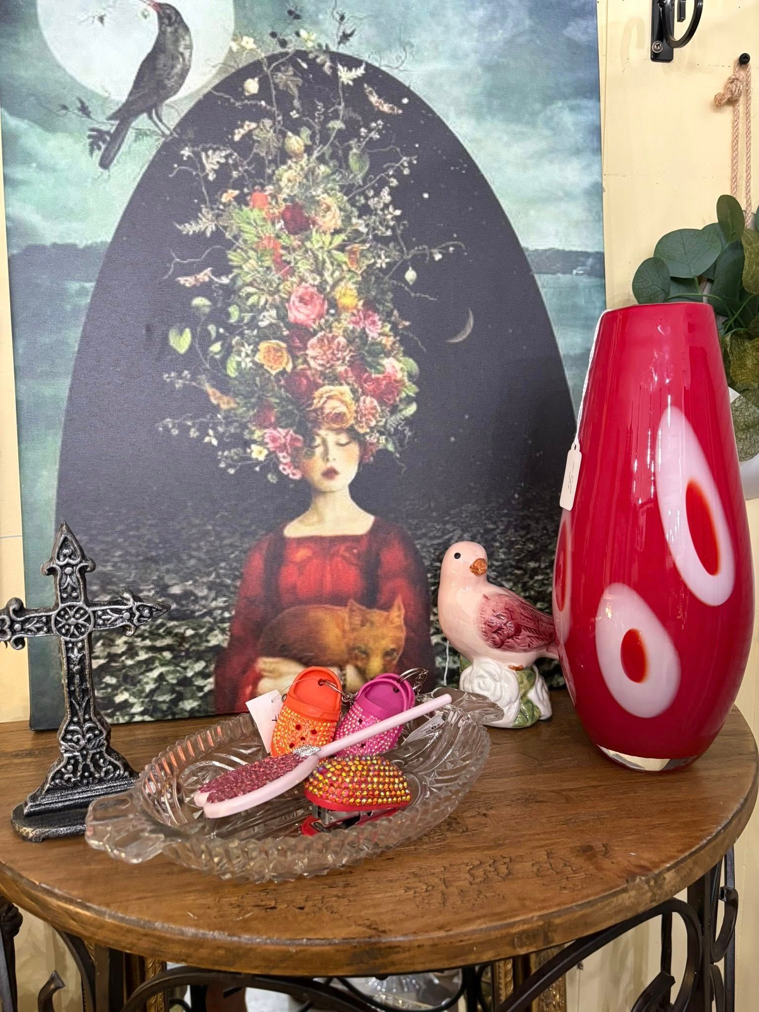 Decorative tabletop with bird figurines, a red vase, fruit, and an abstract portrait backdrop
