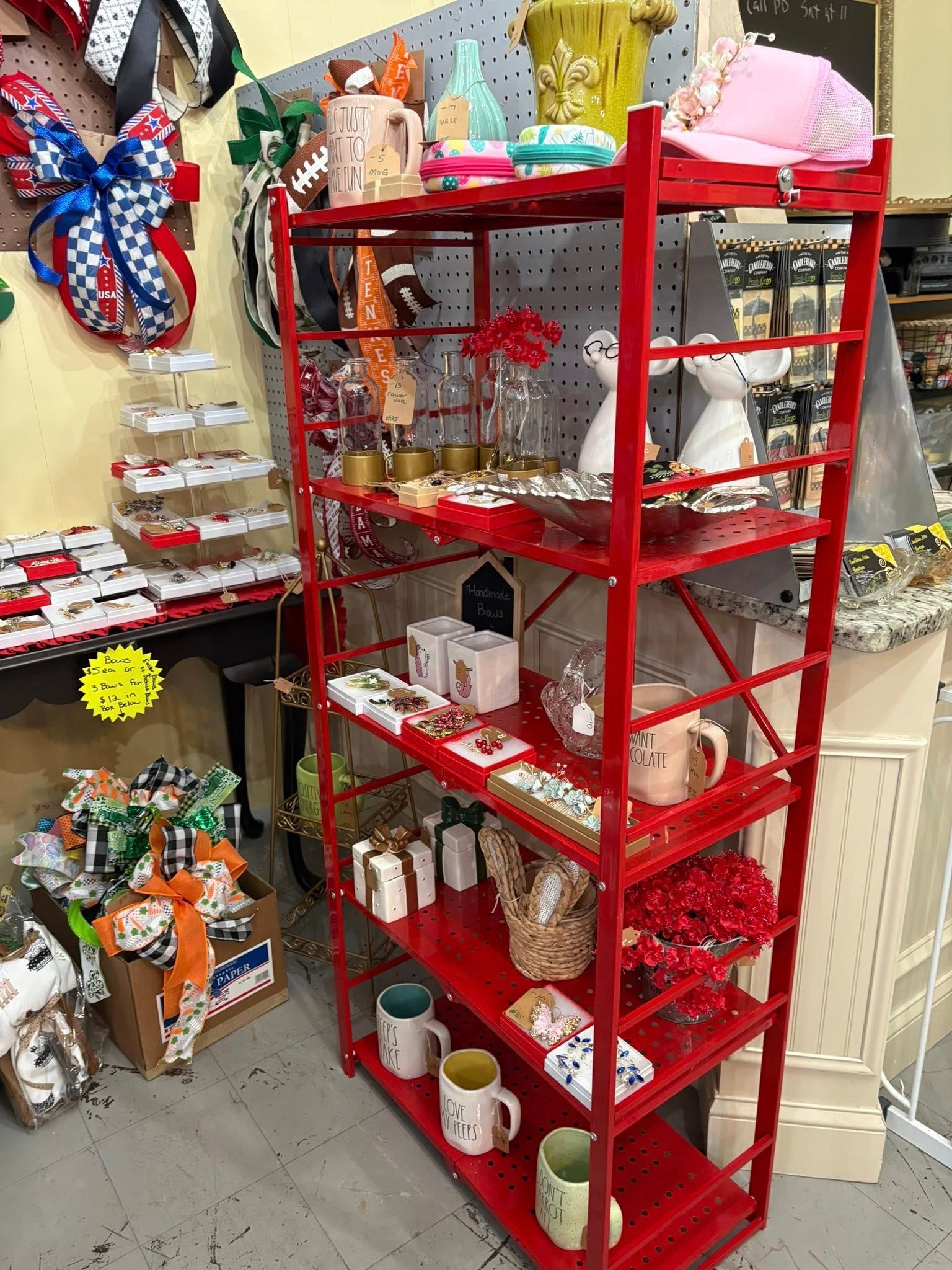 Red metal shelf stocked with mugs, jars, and decor in a cluttered shop corner