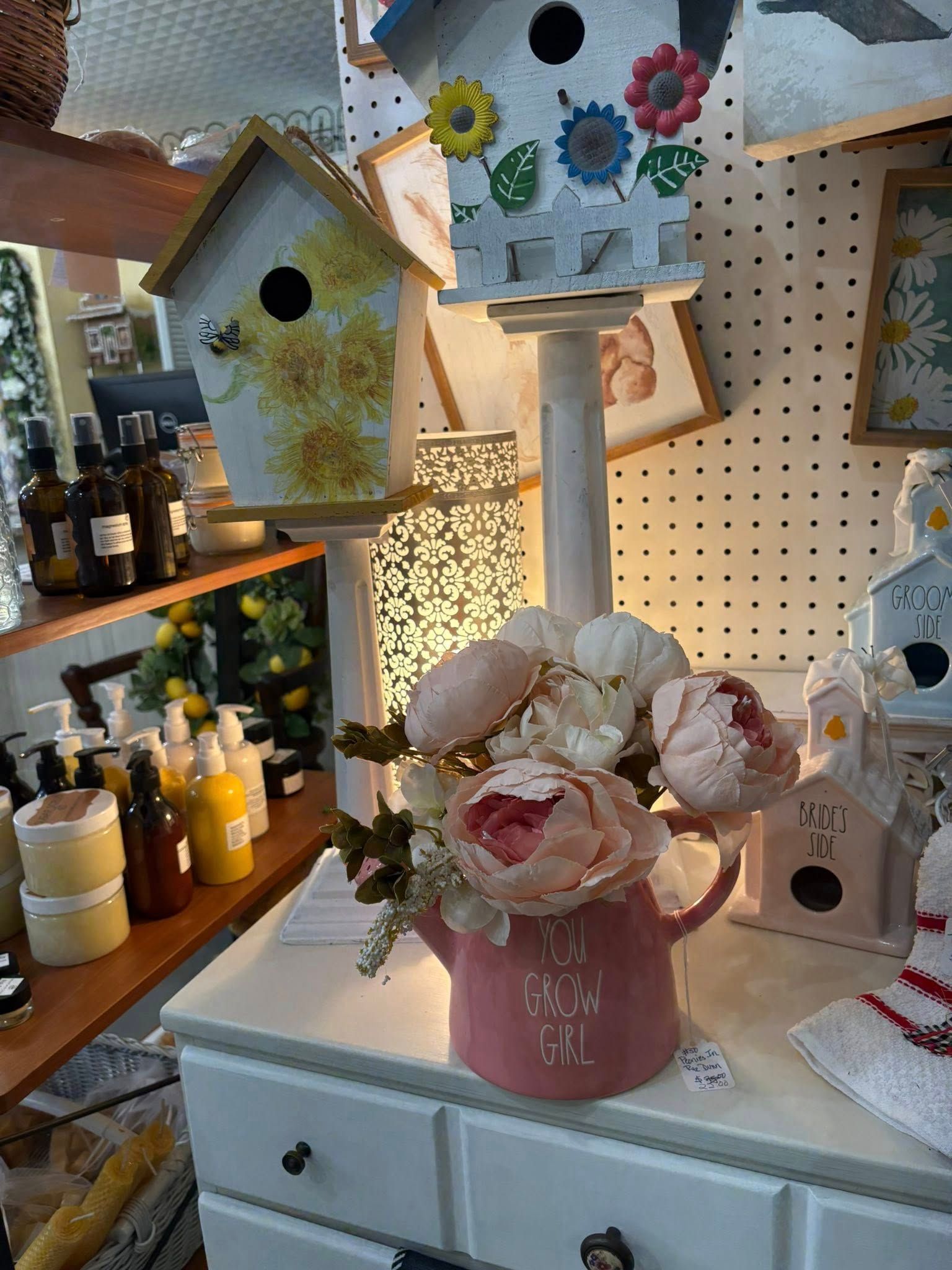 Decorative floral display with pastel birdhouses, painted flowers, and candles on a shop counter