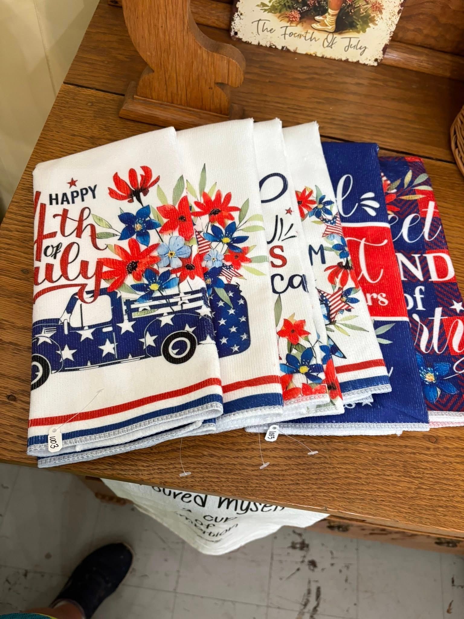 Stack of folded patriotic kitchen towels with red, white, and blue stars and text on a wooden table.
