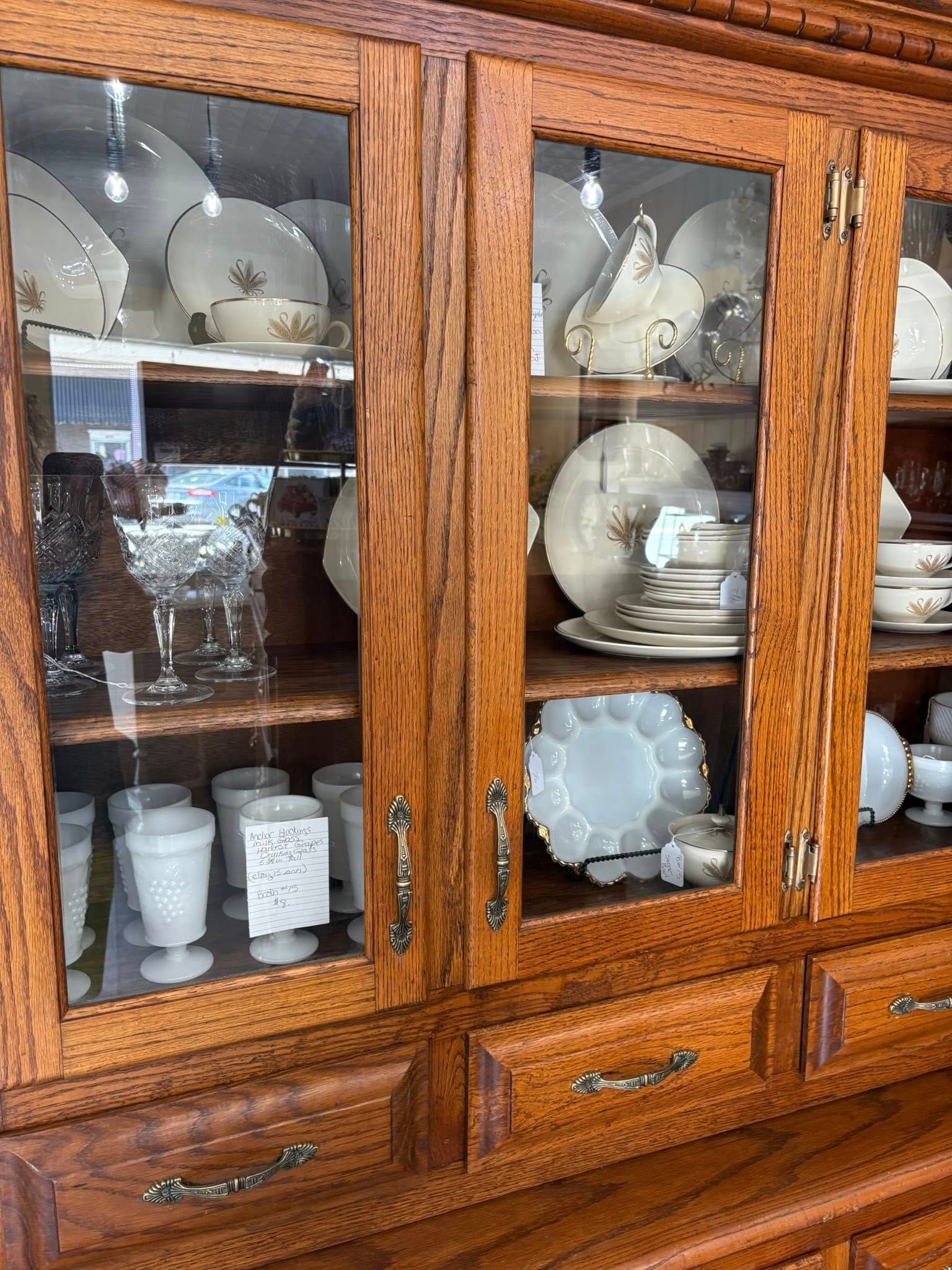 Wooden display cabinet with glass doors holding white dishes and cups