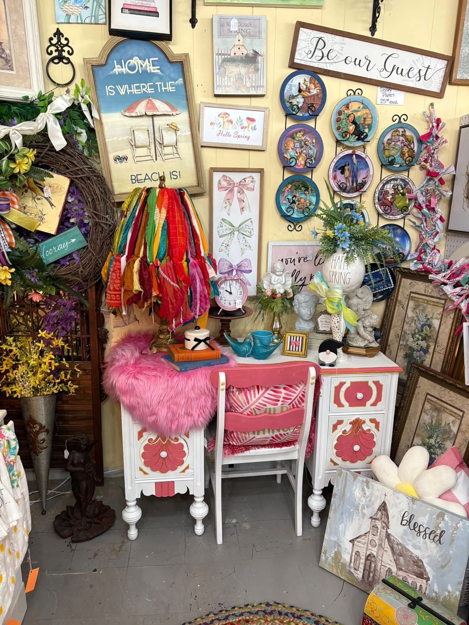 Colorful craft nook with framed art, ribbons, floral decor, and a pink chair under a small desk