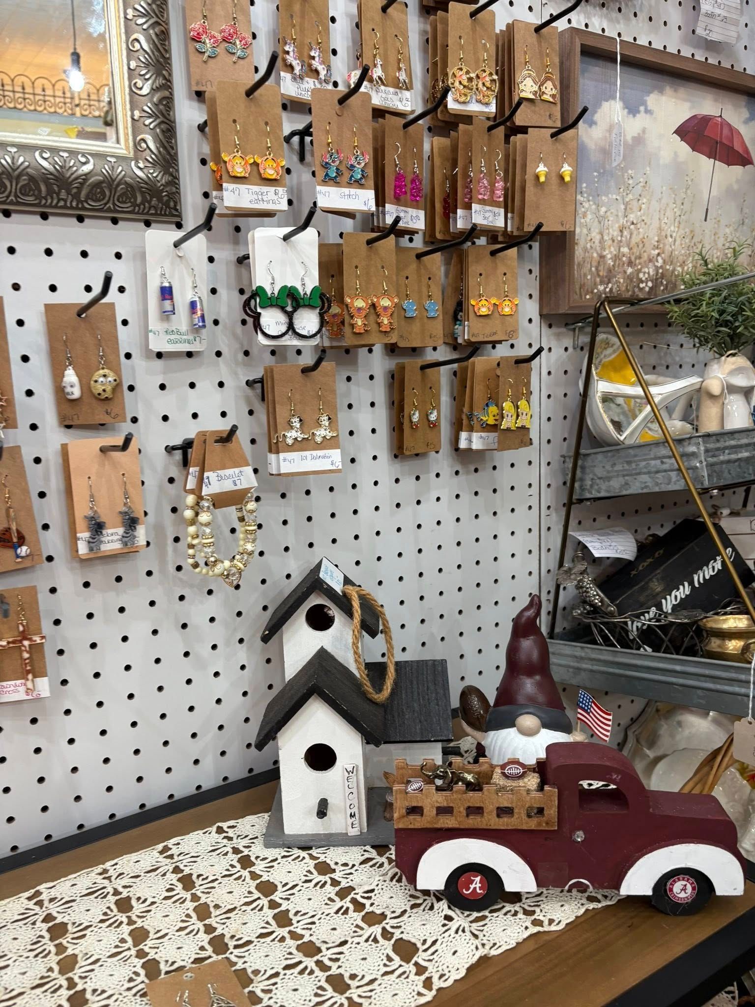 Craft booth display with pegboard art, a white birdhouse, and a red toy truck on a patterned tablecloth.