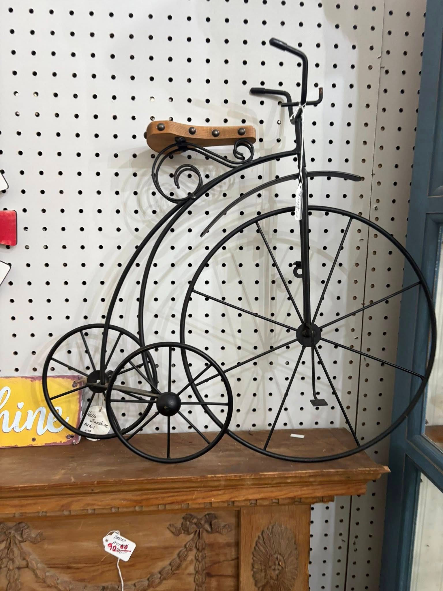 Vintage penny-farthing bicycle on a wooden table in front of a pegboard wall.