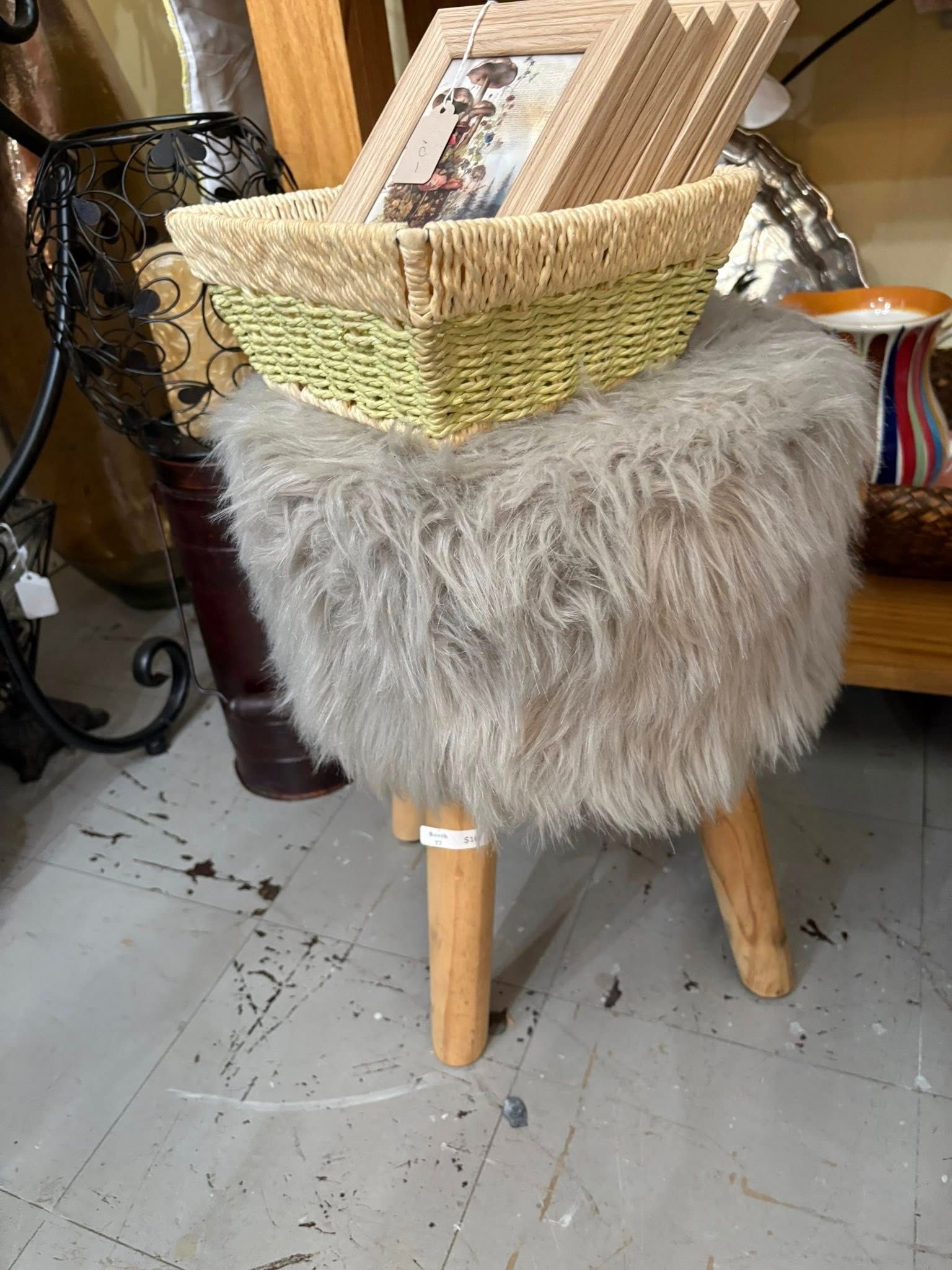 Wicker basket chair with wooden legs and a fluffy gray cover in a shop display.