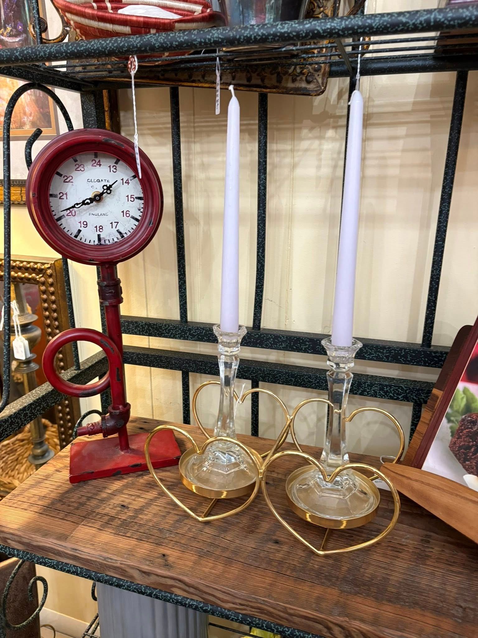 Vintage red clock beside two white candles in brass holders on a shelf