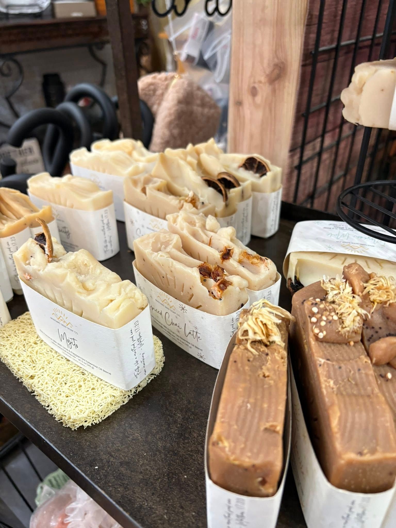 Assorted soap bars in paper wrappers displayed on a market table, including tan and cream swirled bars.