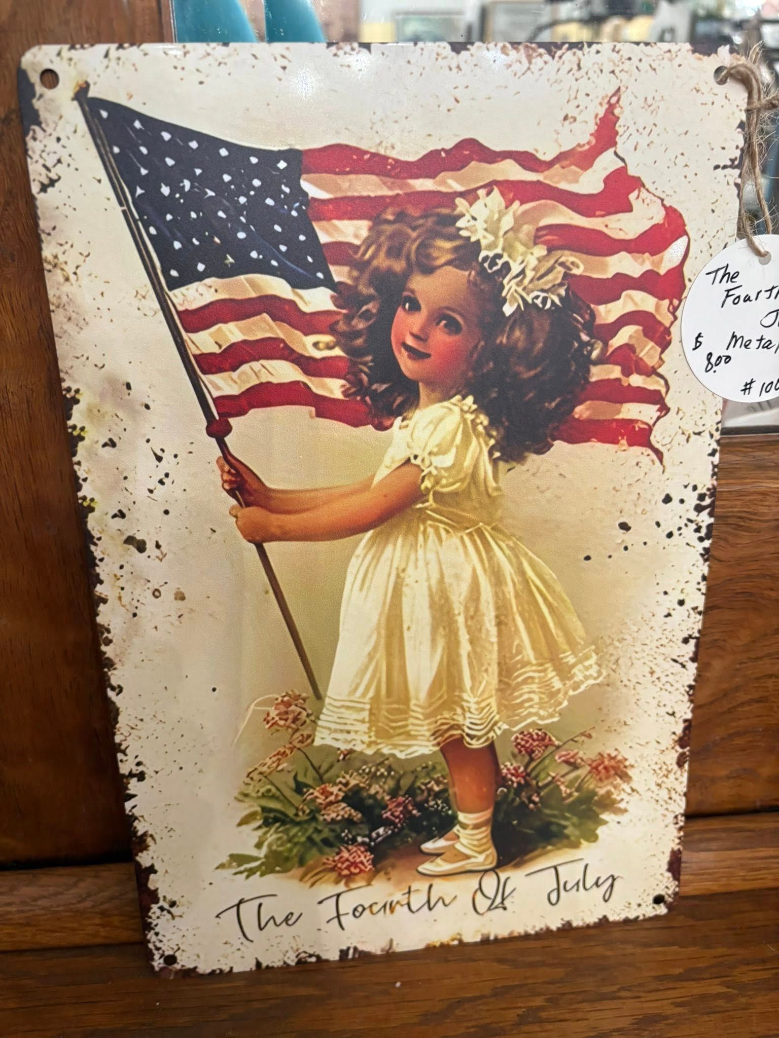 Girl holding an American flag, with “The Fourth of July” written below.