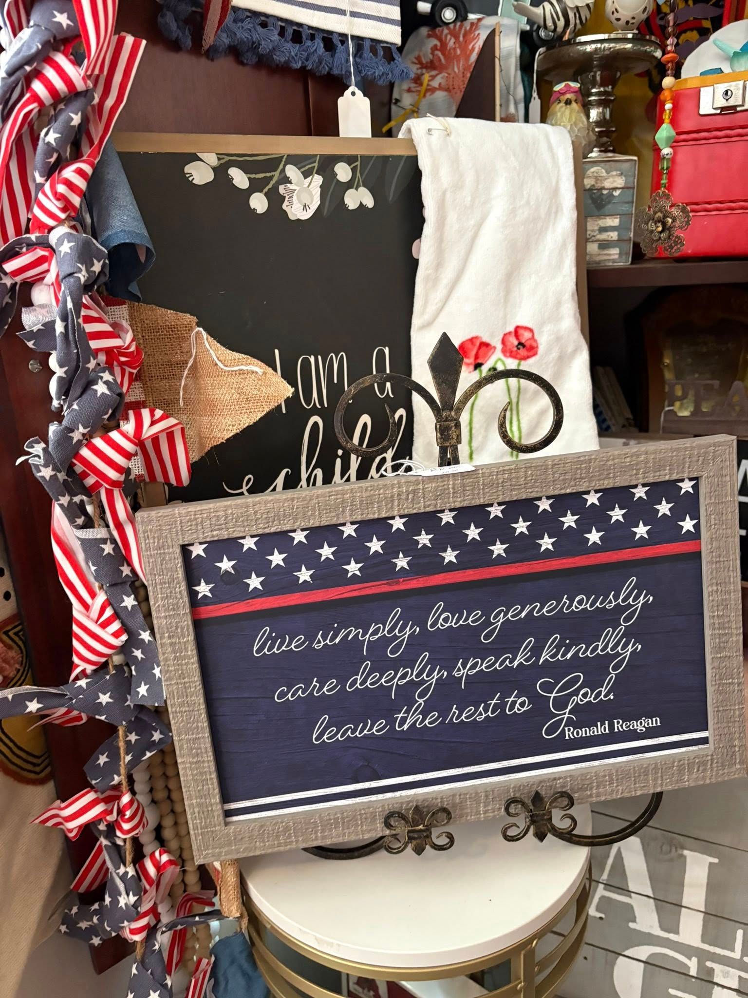 Patriotic chalkboard sign with stars-and-stripes border, hanging on a red, white, and blue ribbon display