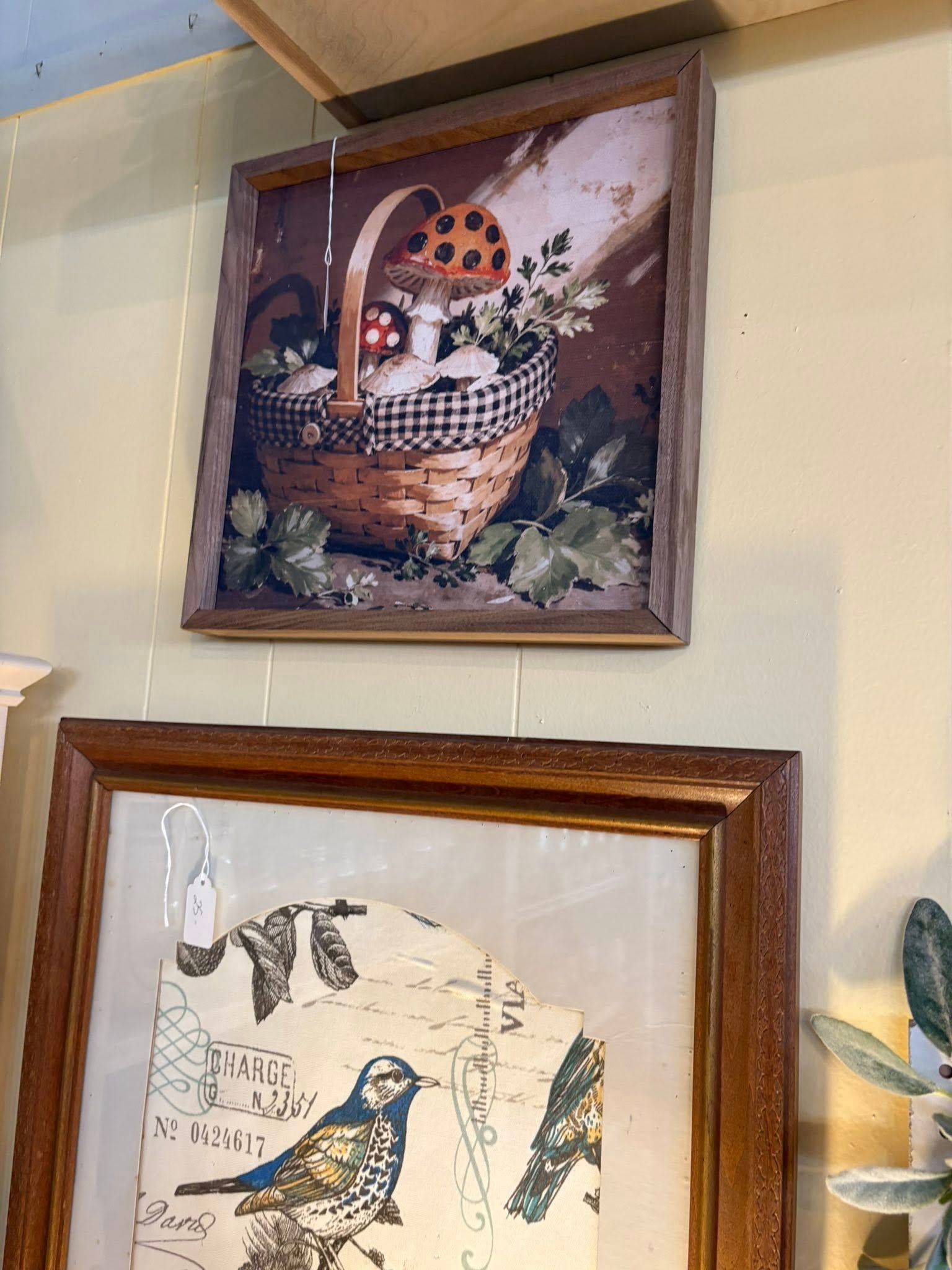 Two framed bird prints hang on a light wall, one featuring a basket with oranges.