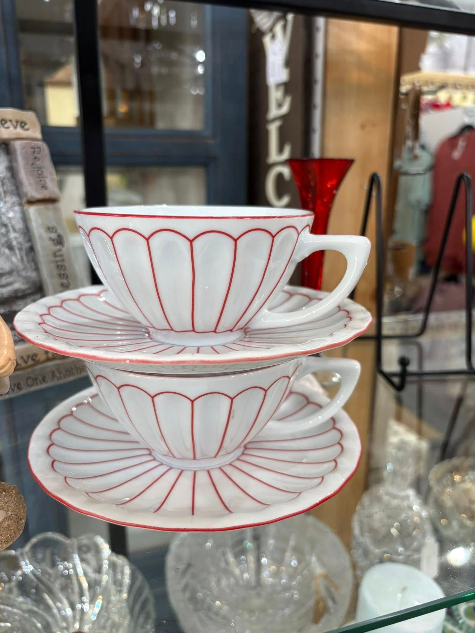 Stacked white teacups and saucers with red scalloped and radial patterns on a display shelf