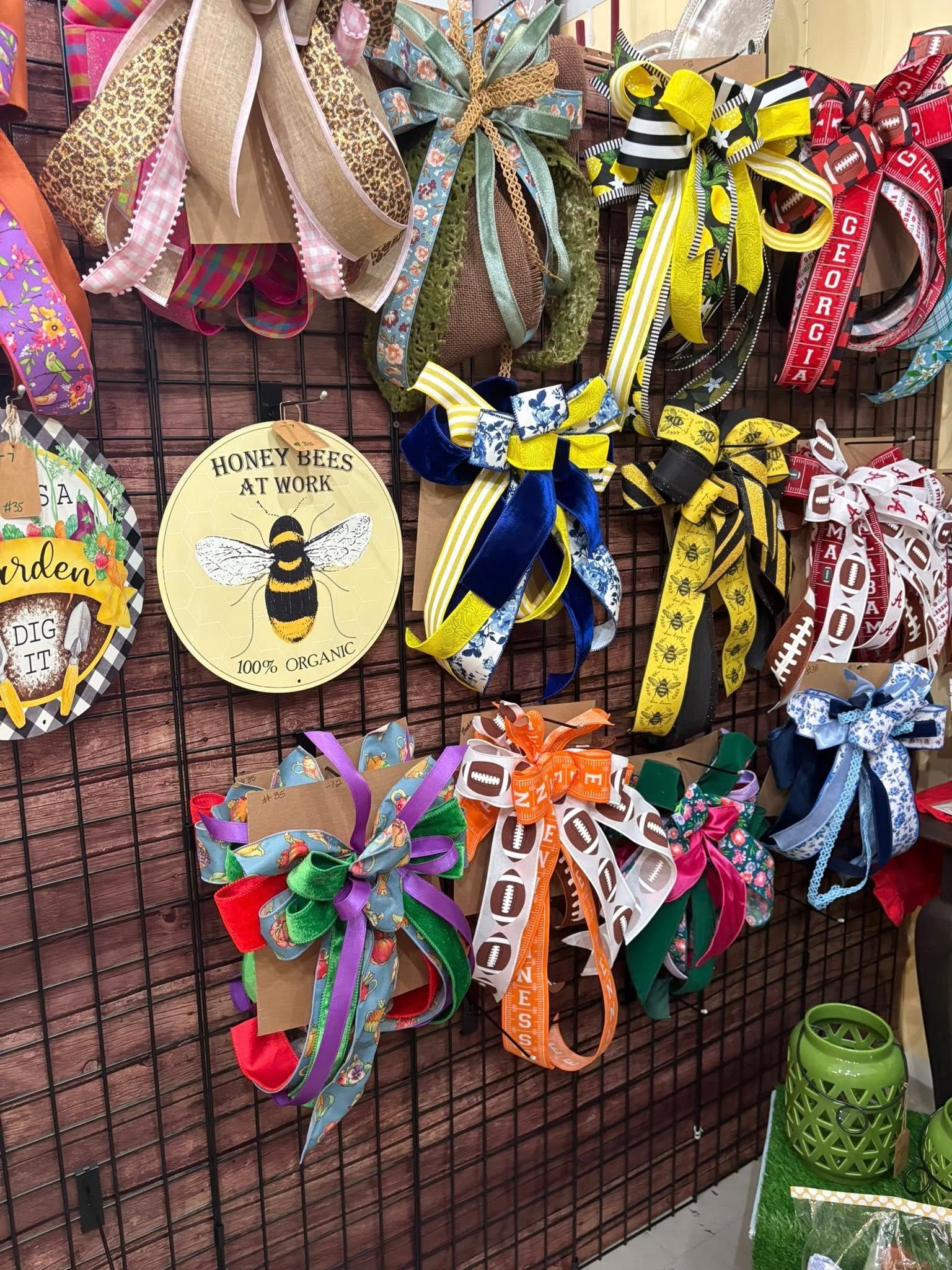 Colorful ribbon wreaths and decorative swags displayed on a wire grid at an outdoor market stall