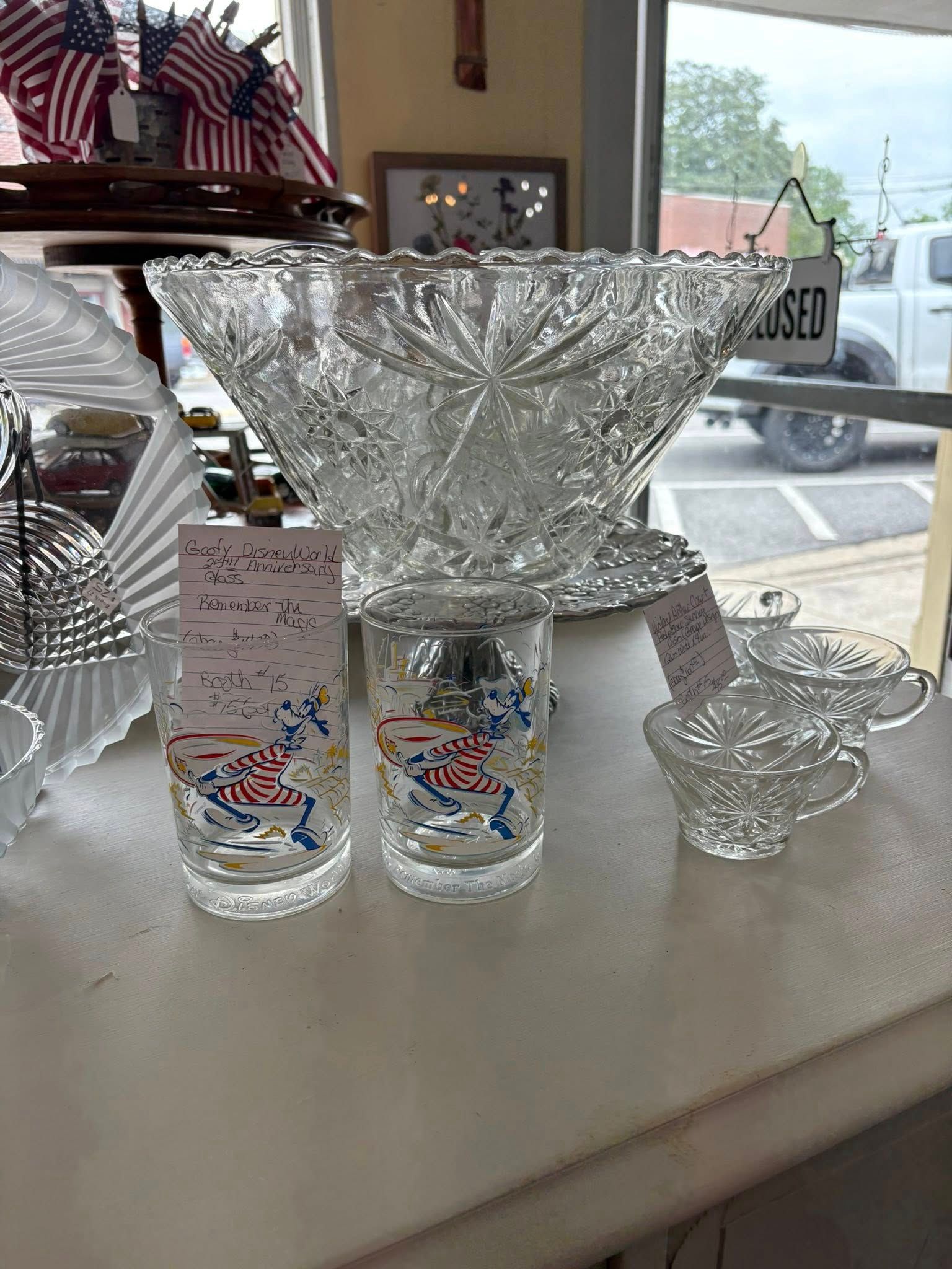 Glass bowl, cups, and a small pitcher displayed on a store counter near a window.
