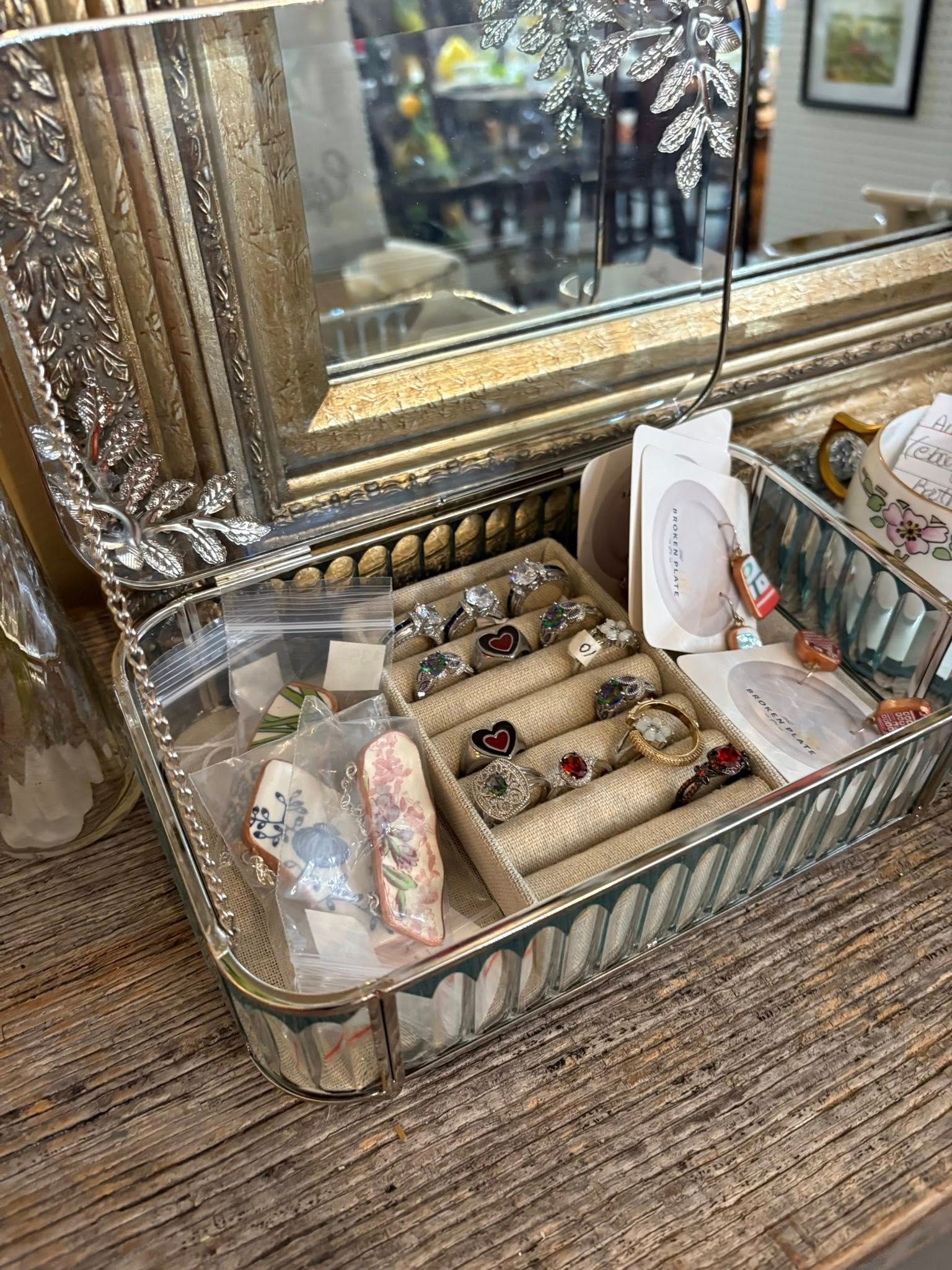 Decorative vanity tray with jewelry and a tissue box on a countertop beside a mirror.