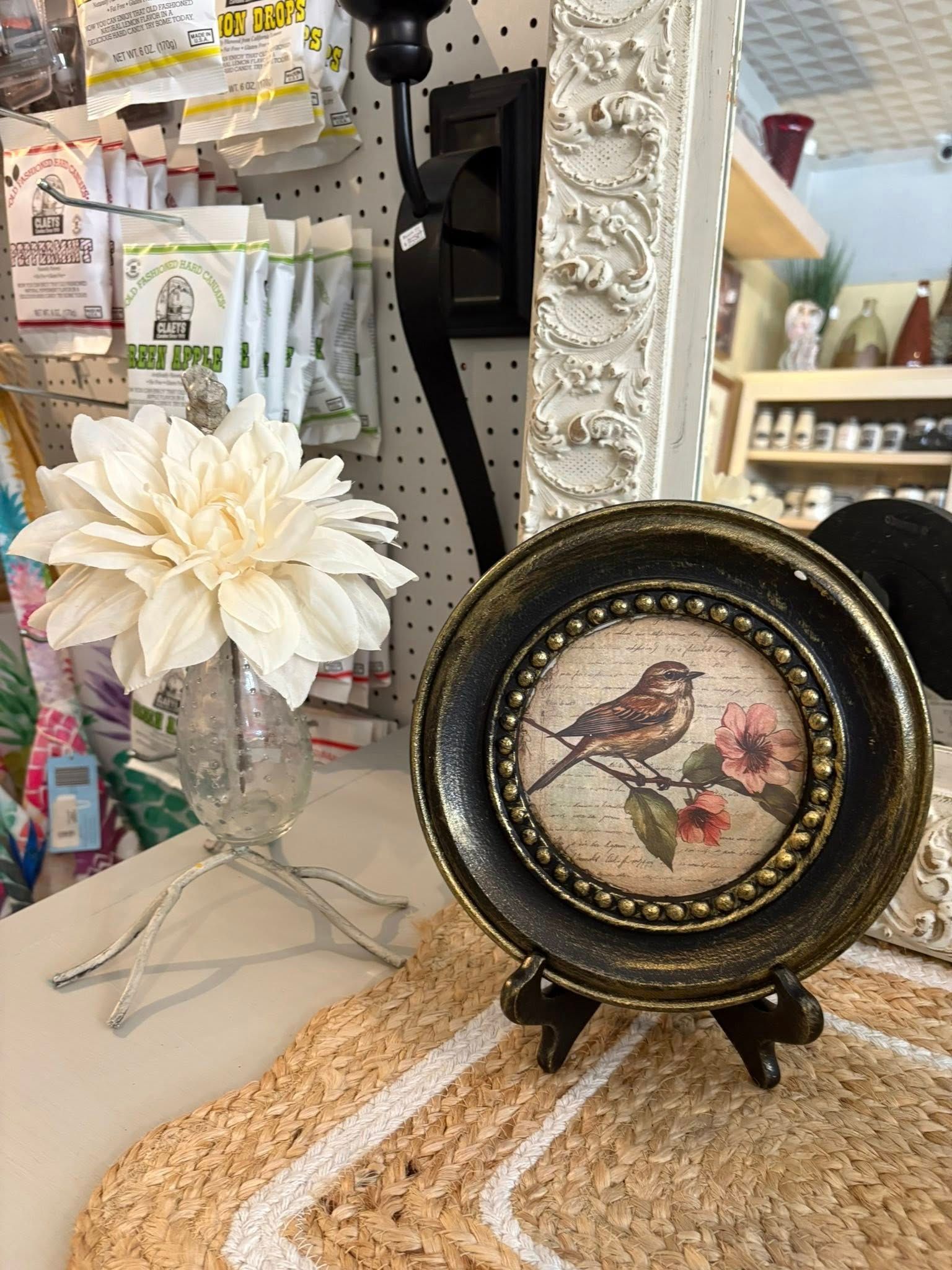 Decorative round bird plaque on a store display shelf beside a large cream flower decoration