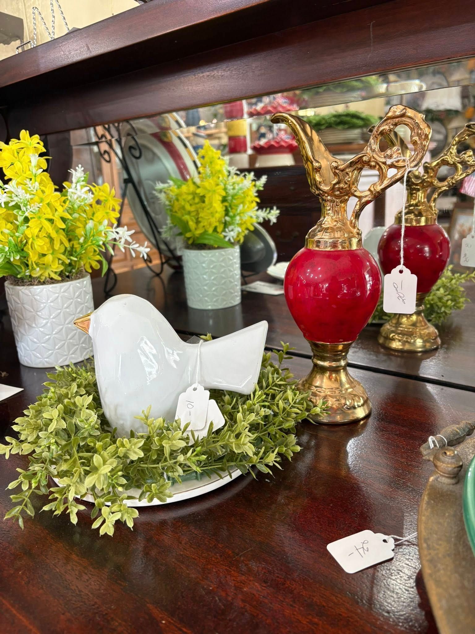 Decorative tabletop display with white bird figurine, red glass ornaments, and small yellow potted flowers