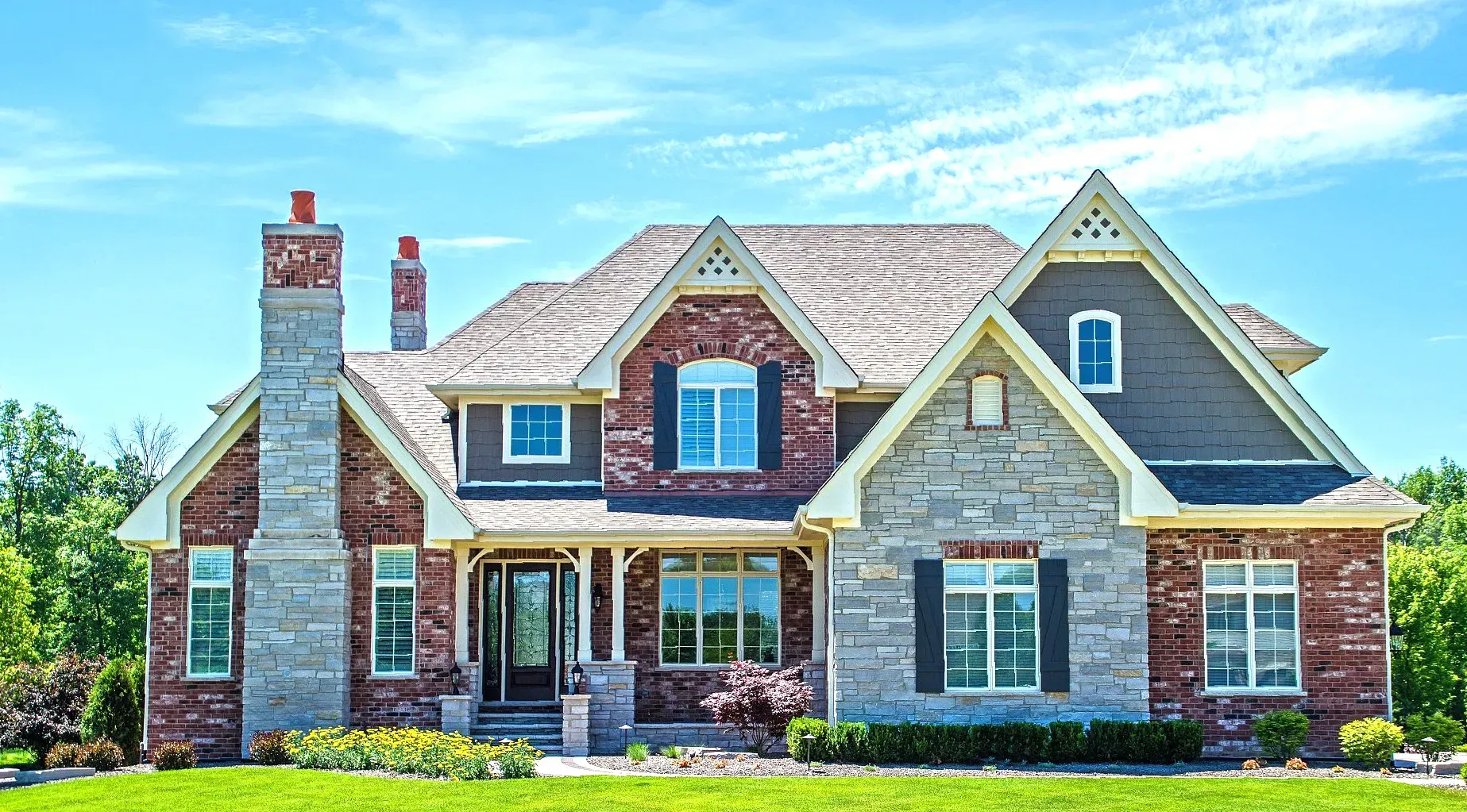 A large brick and stone house with a blue sky in the background.