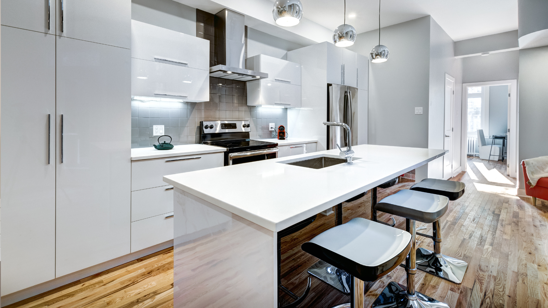 A kitchen with white cabinets , a large island , stools and a stove.
