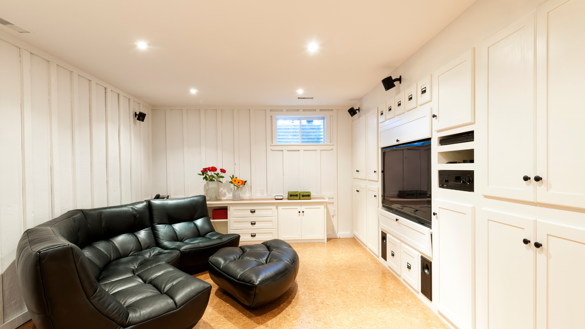 A living room with a black couch , ottoman , and television.