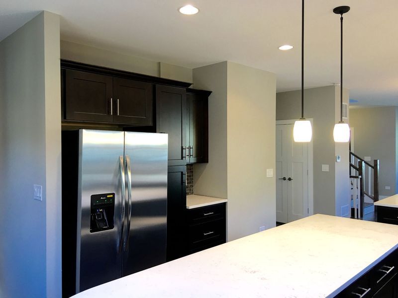 A kitchen with black cabinets and a stainless steel refrigerator