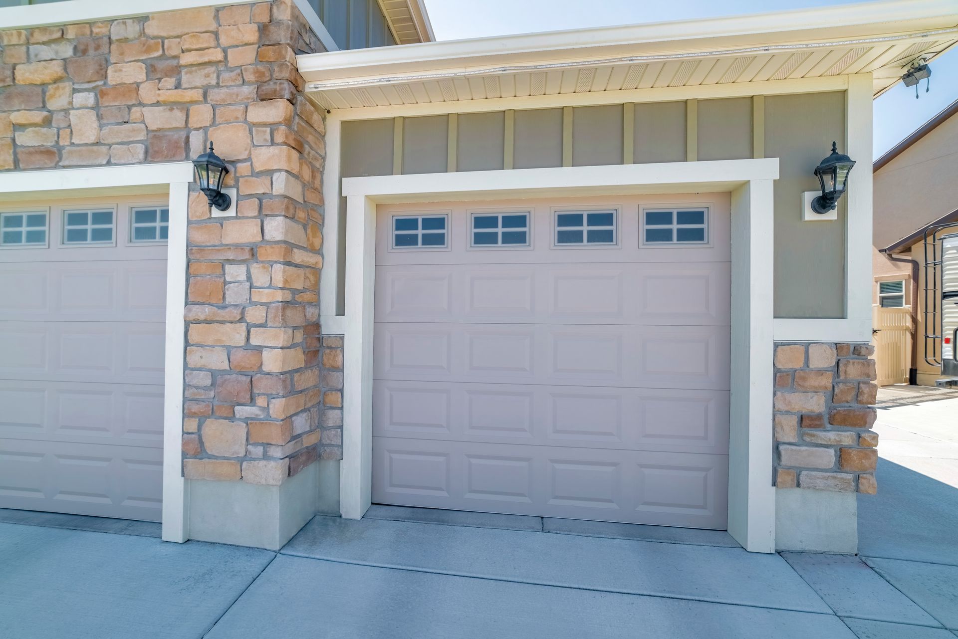 A closed residential garage door framed by stone and siding sits in a clean driveway.