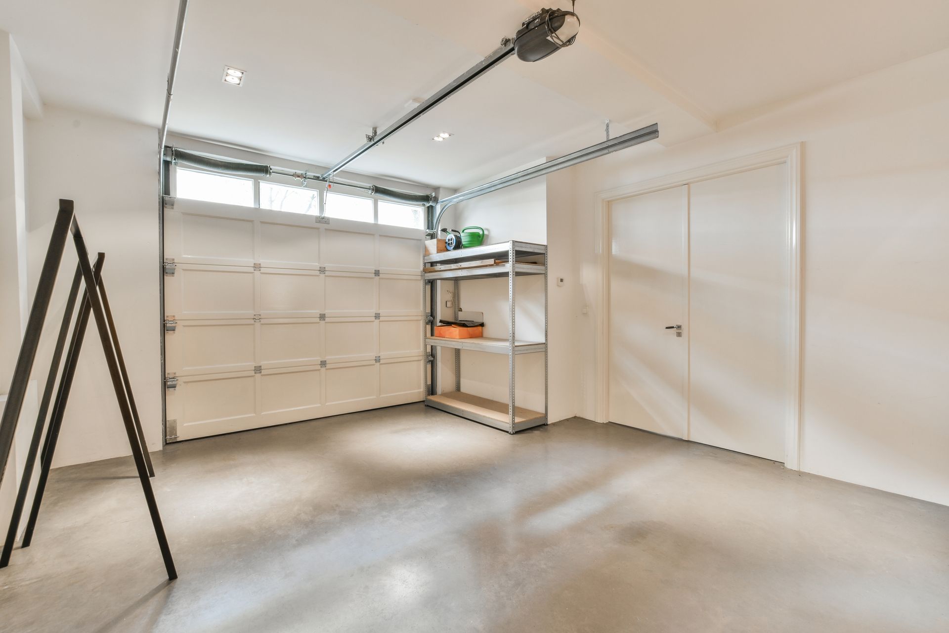 A clean garage interior with a closed overhead door, ceiling opener, and organized shelving.
