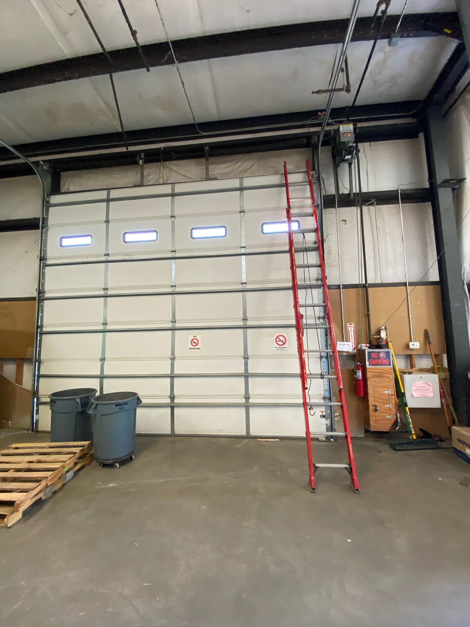 Red ladder leans against a closed, white overhead garage door inside a warehouse. Red ladder leans against a closed, white overhead garage door inside a warehouse.