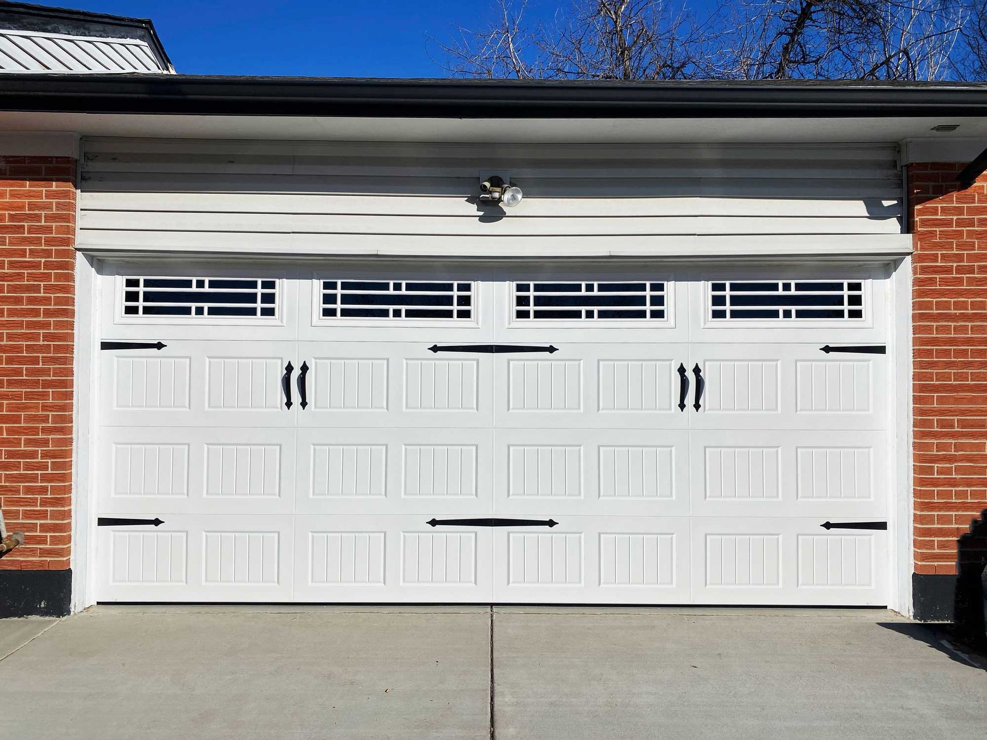 White garage door with black hardware, set in a brick and siding facade.