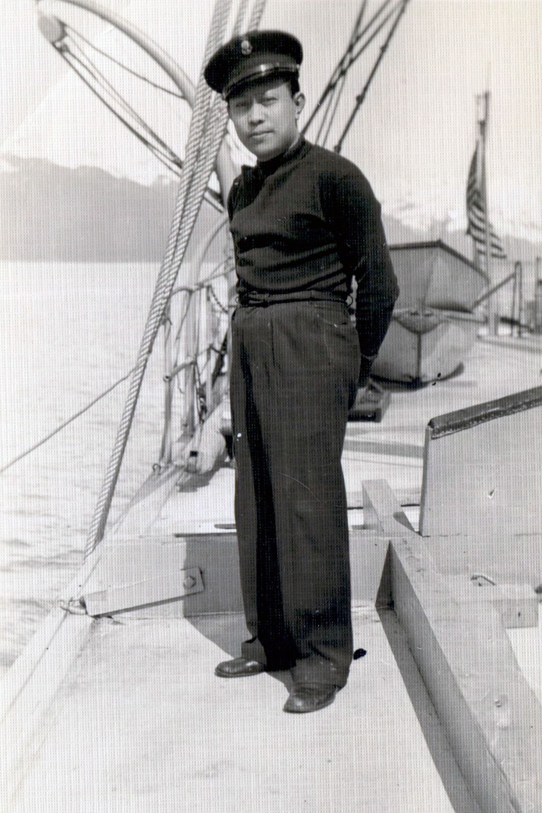 A man in a navy uniform standing on the deck of a boat