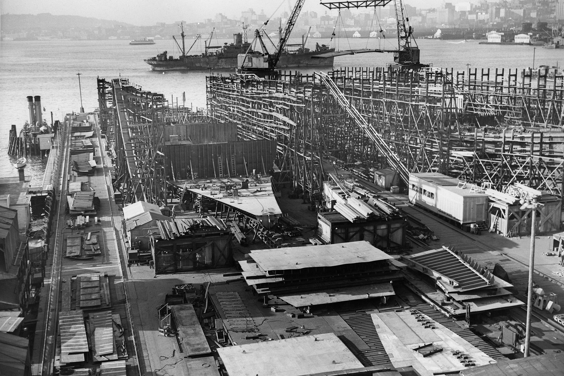 A black and white photo of a shipyard with a large ship in the background
