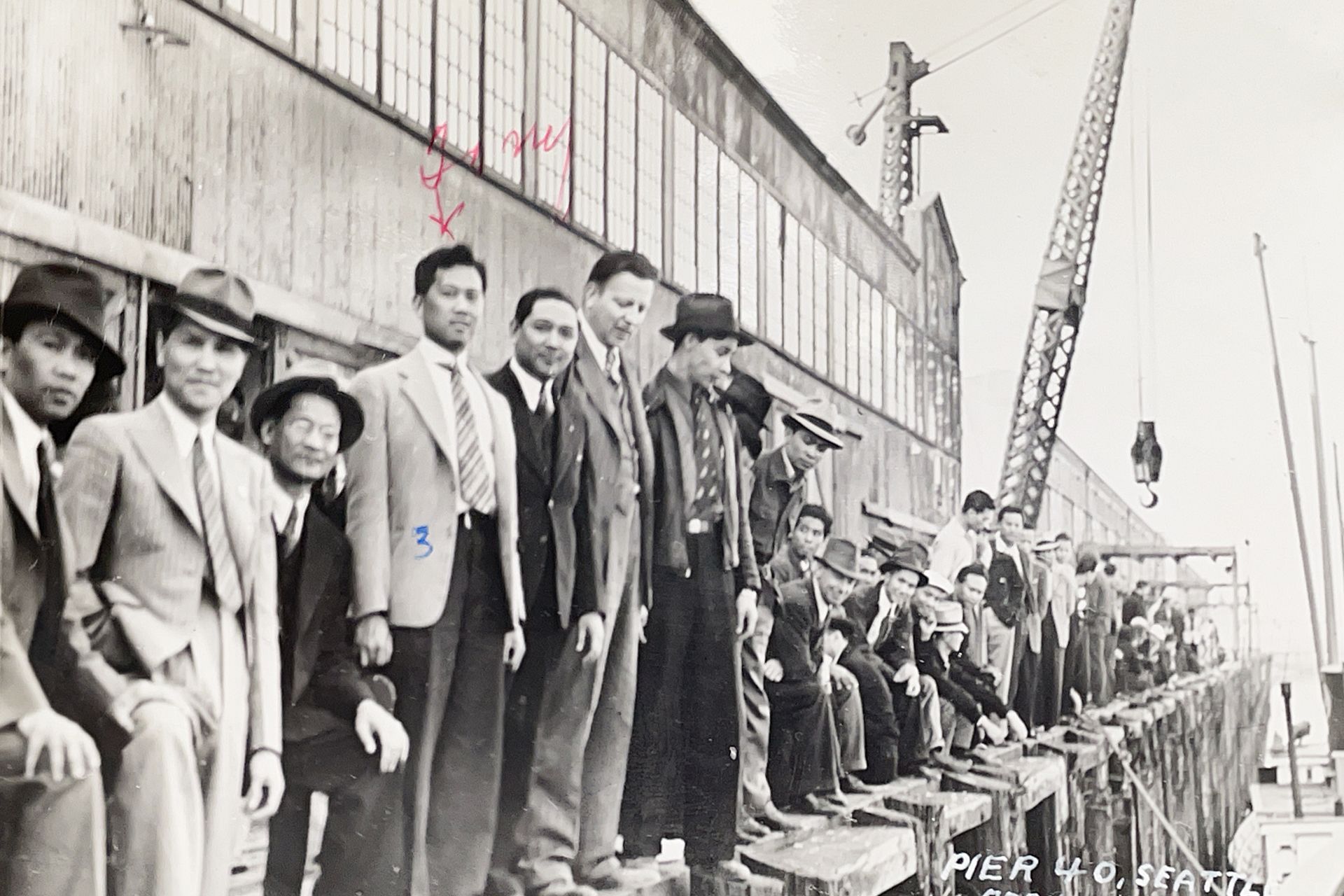 A black and white photo of a group of men standing on a pier