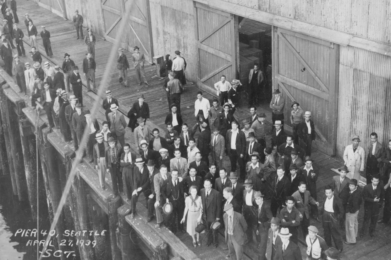 A black and white photo of a large group of people standing on a pier