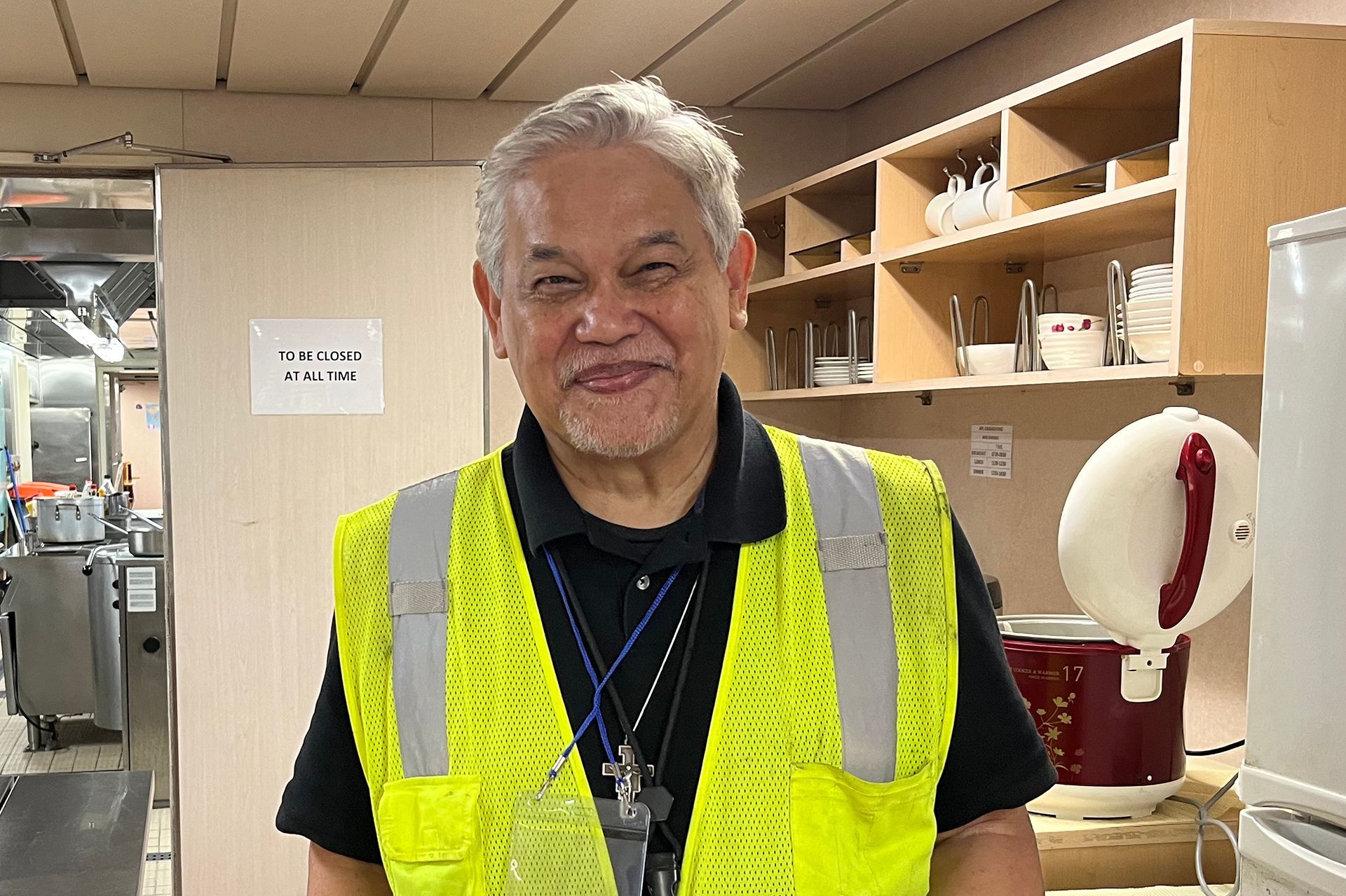 A man wearing a yellow safety vest stands in a kitchen
