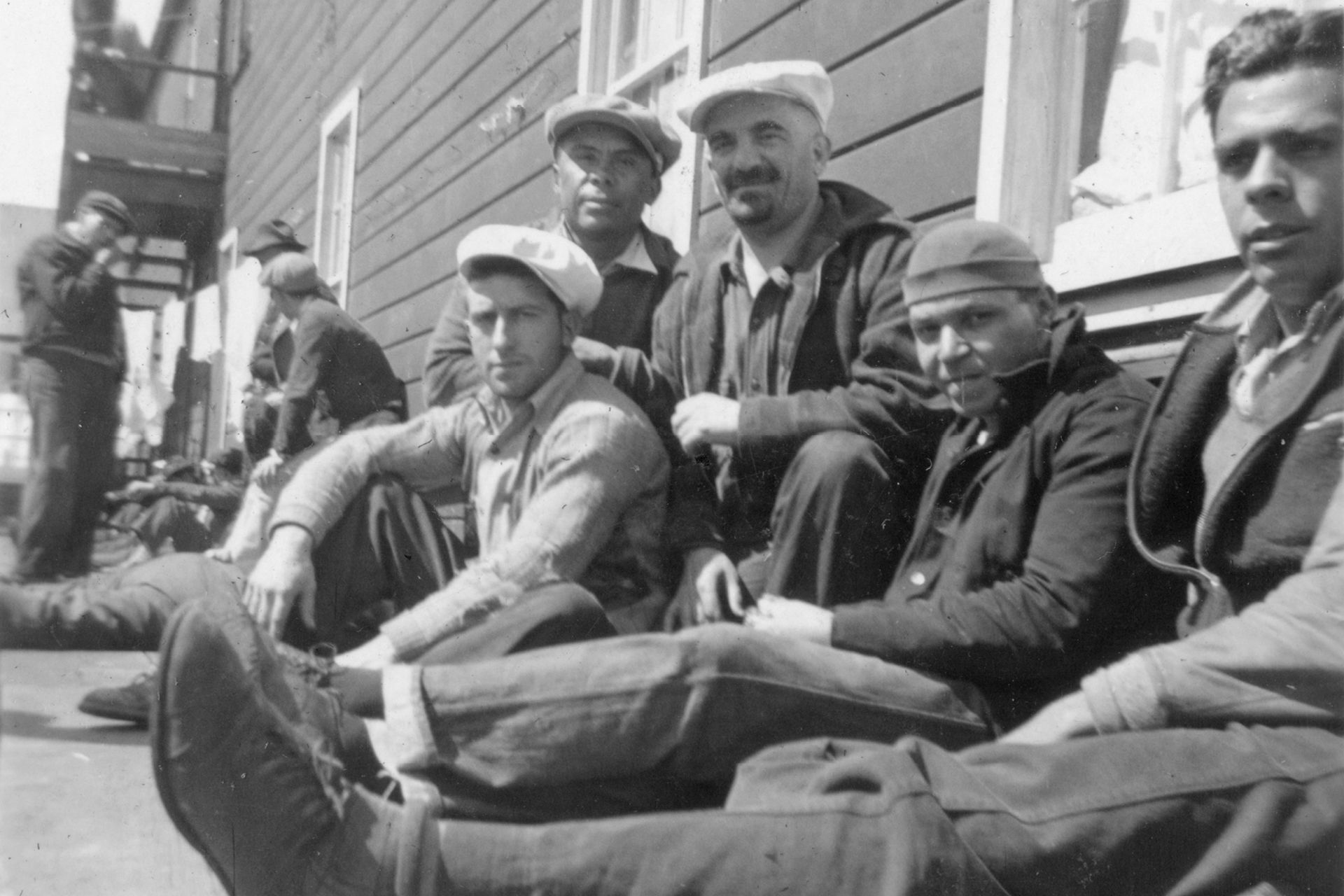 A group of men sitting on the sidewalk in front of a building on a pier