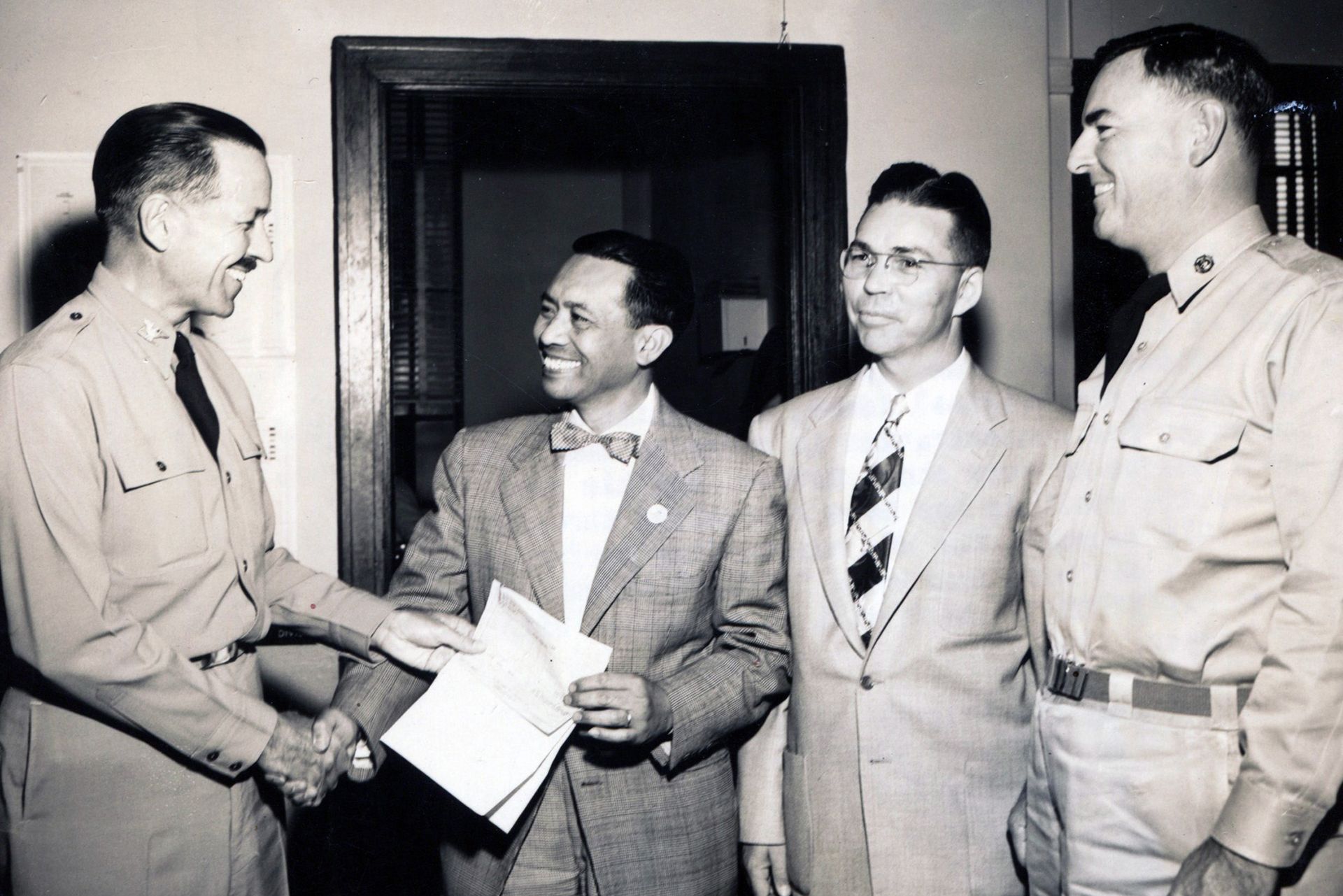 A black and white photo of four men shaking hands