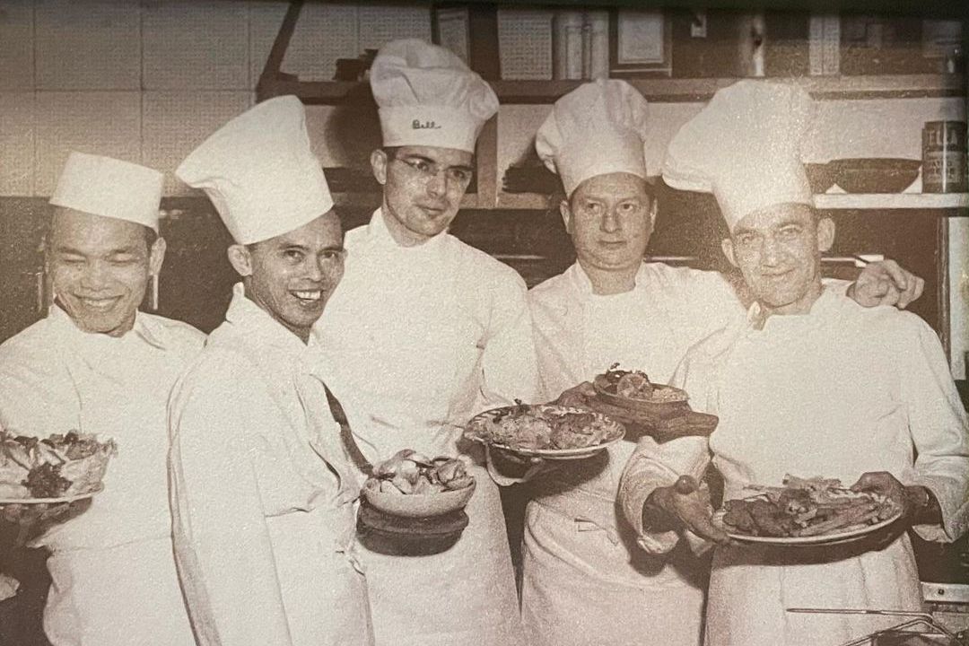 A black and white photo of five chefs holding plates of food