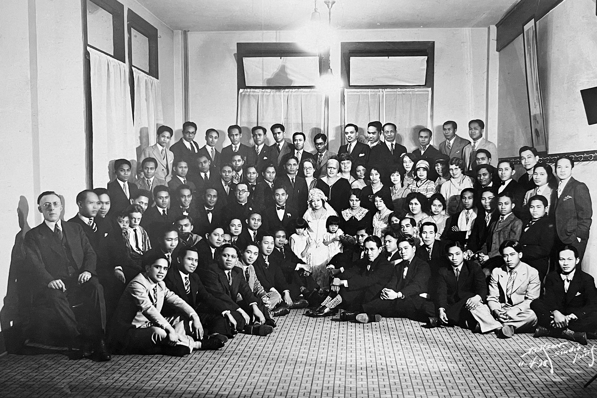 A black and white photo of a large group of people gathered around a couple in bridal dress