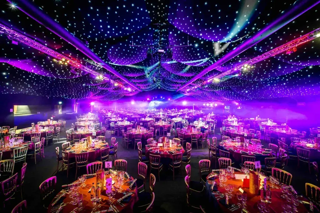 A large room filled with tables and chairs with purple lights on the ceiling.