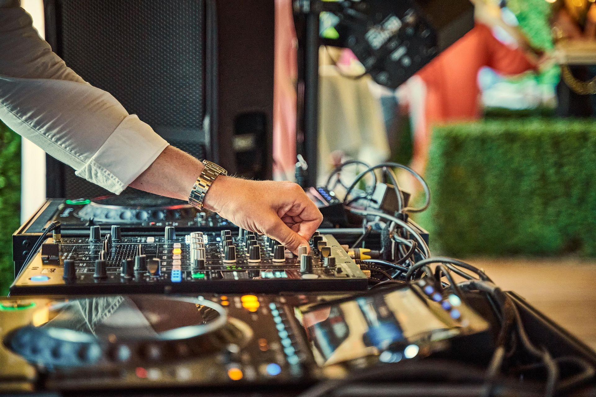 DJ adjusting controls on a mixer with cables in a colorful indoor event setting