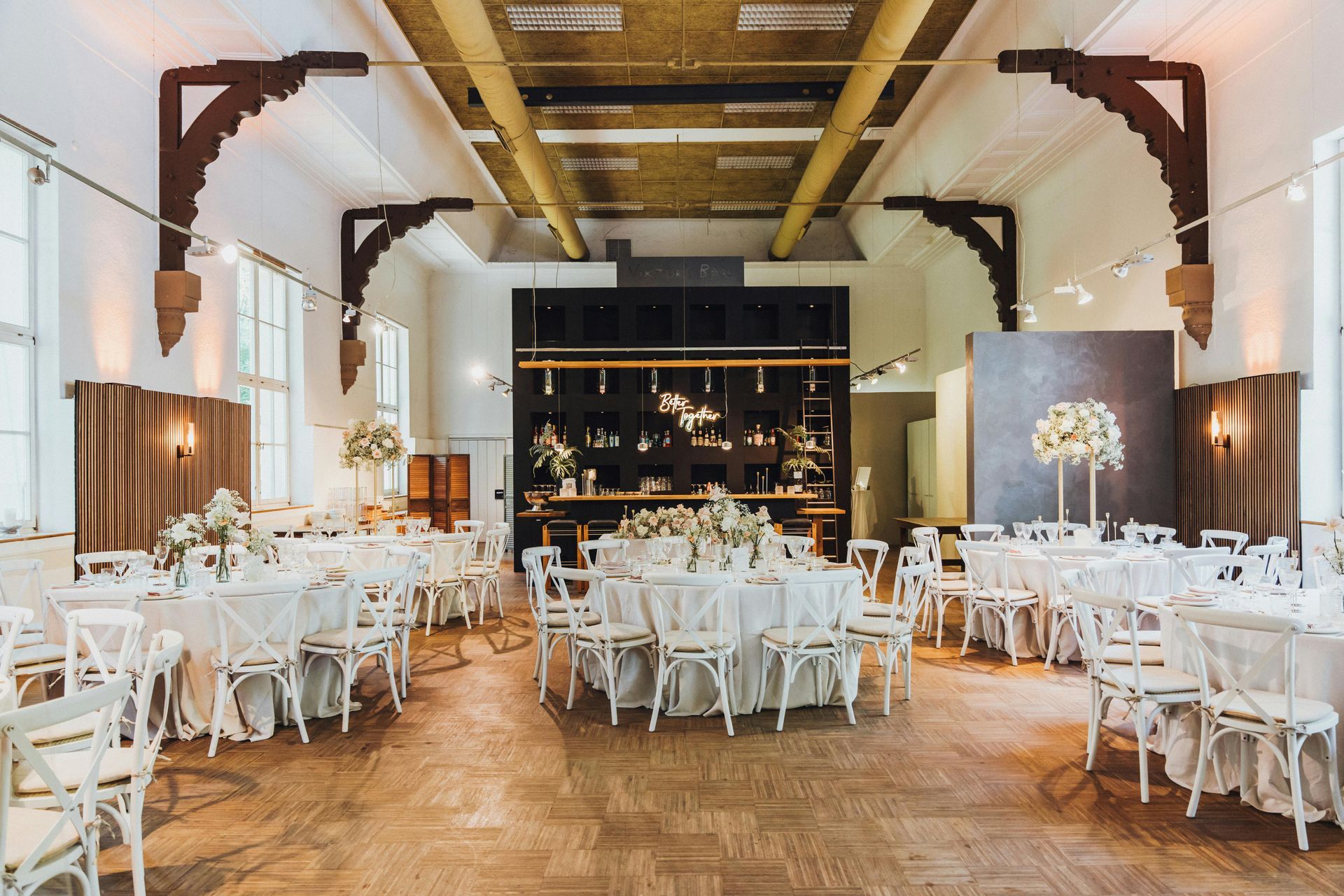 Elegant banquet hall with white round tables, chairs, wooden floors, and warm ceiling lights