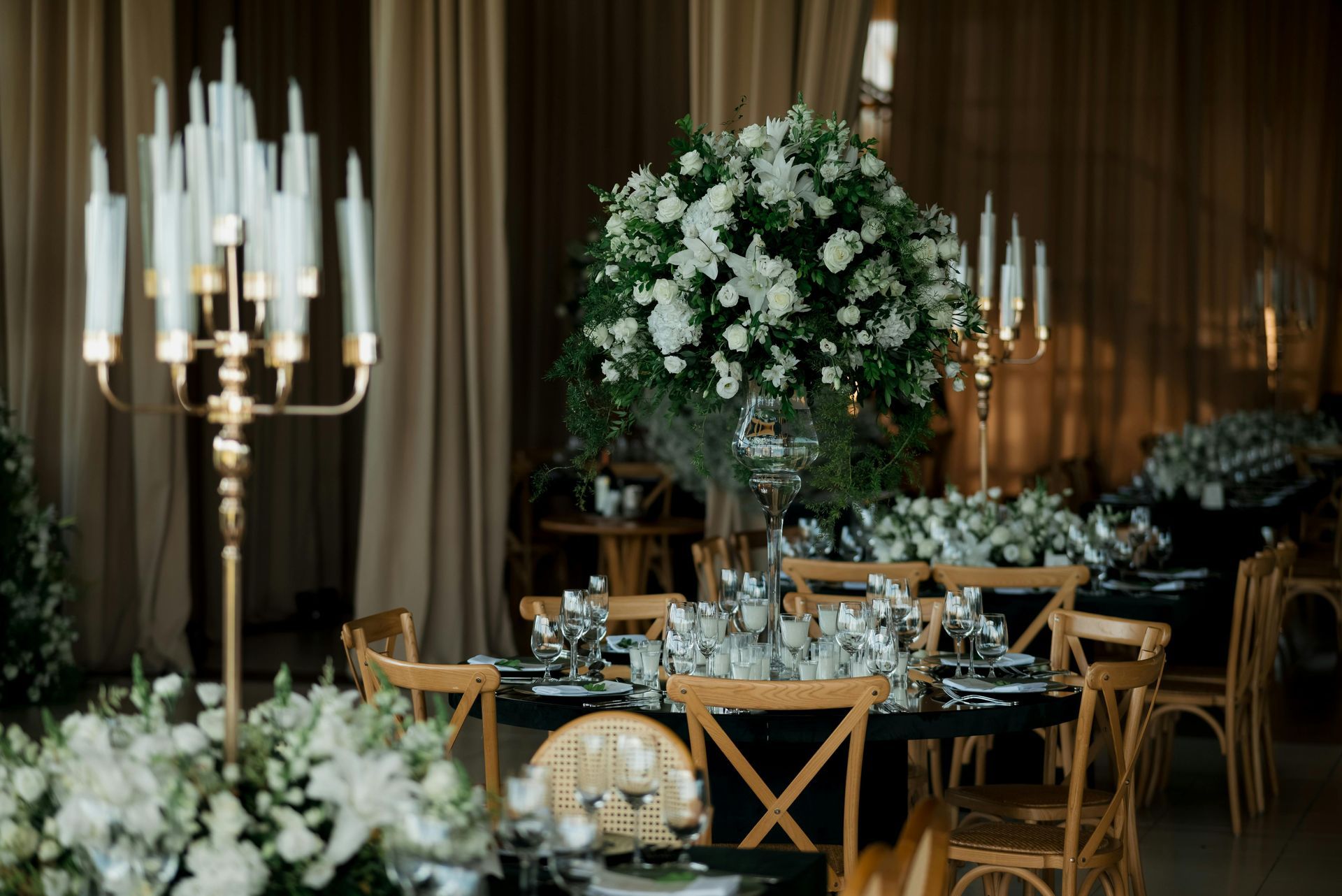 Elegant wedding reception tables with gold chairs, white floral centerpieces, and candlelit decor