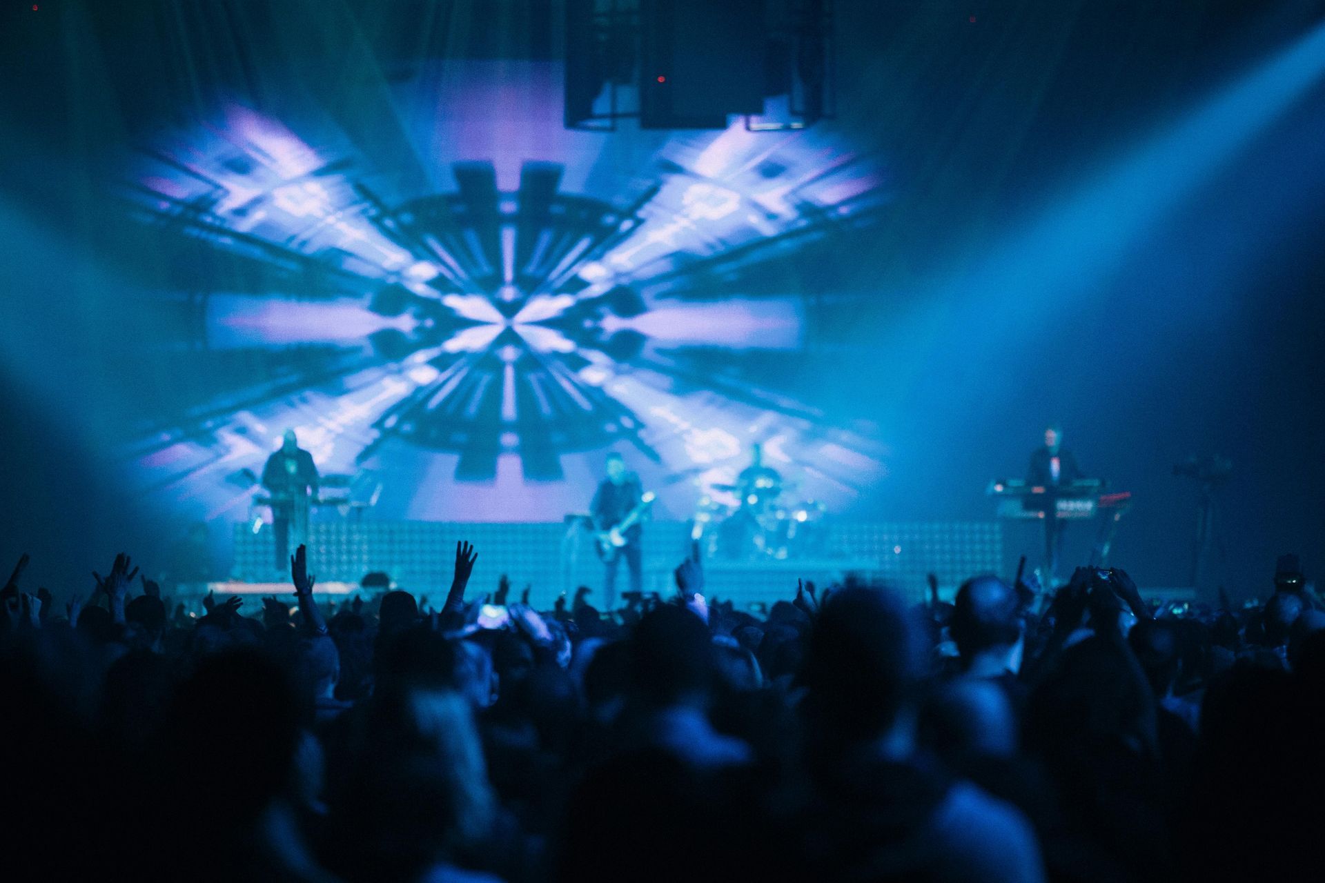Concert crowd watching a blue-lit stage with bright abstract visuals and musicians performing