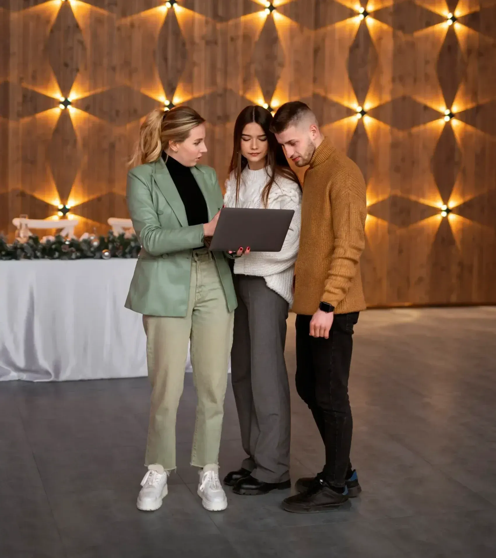 A man and two women are standing next to each other looking at a laptop.