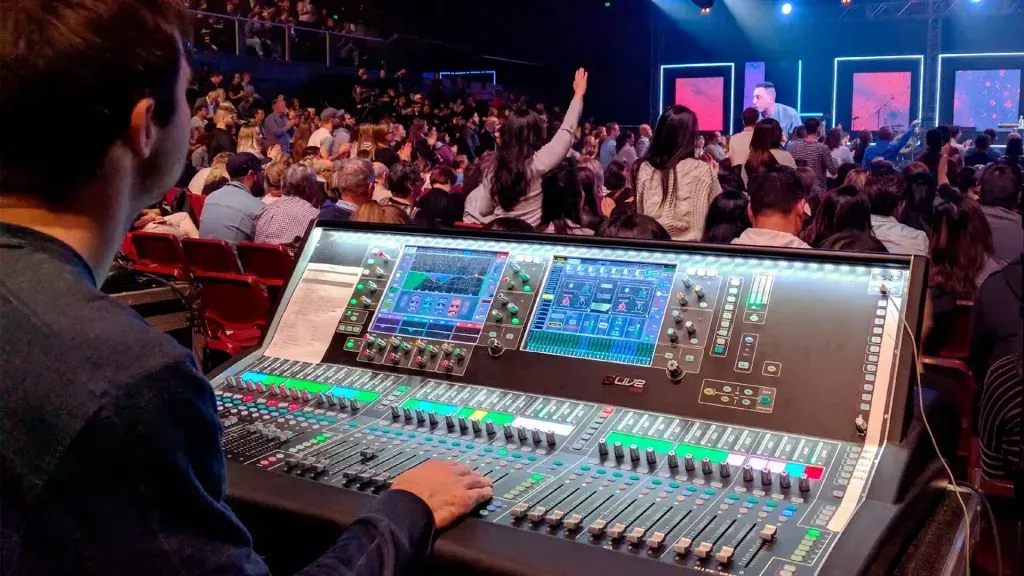 A man is sitting at a mixer in front of a crowd of people.