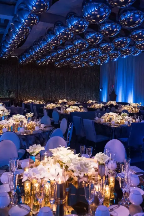 A large room with tables and chairs set up for a party with blue balloons hanging from the ceiling.