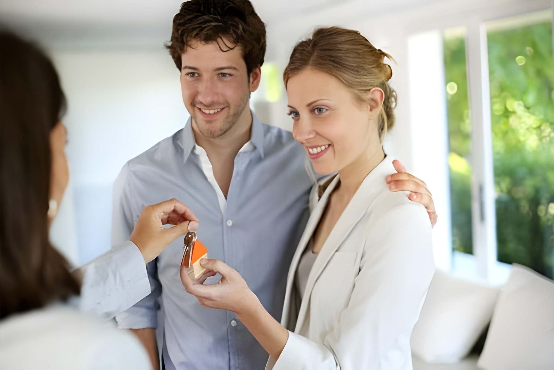 Woman Handing House Keys to Smiling Couple Indoors — Peterson Property Valuations Brisbane in Gold Coast, QLD