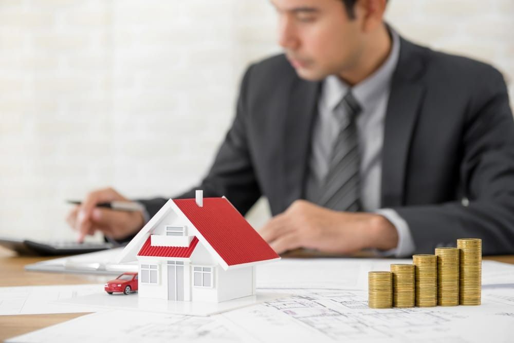 Man in Suit Calculating With House Model — Peterson Property Valuations Brisbane in Caloundra West, QLD
