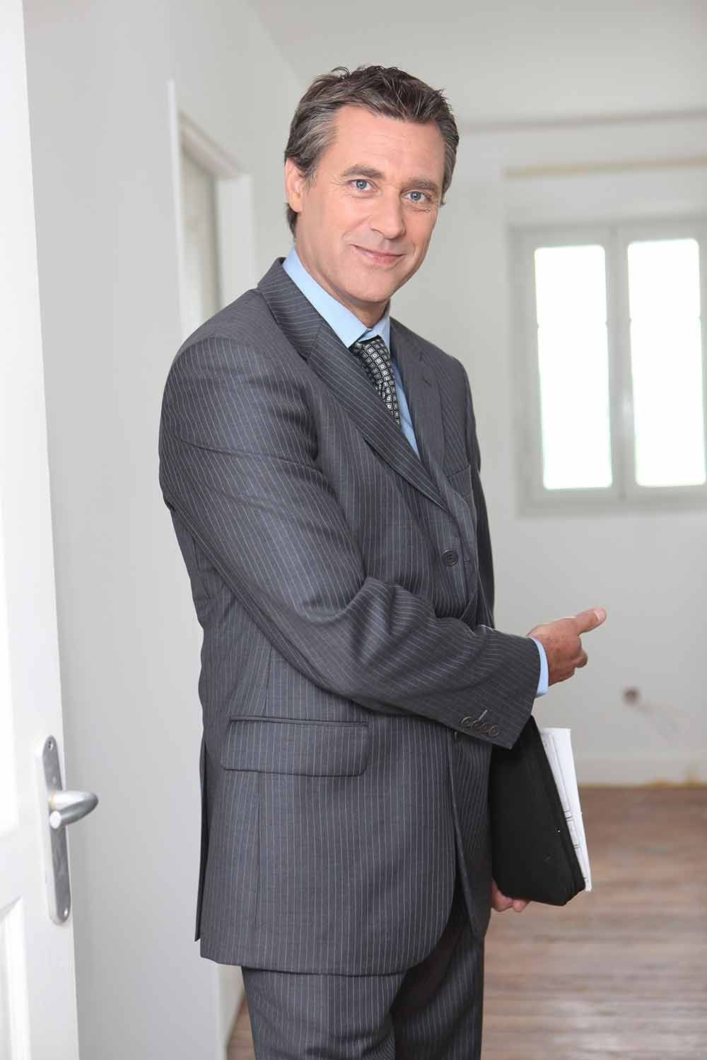 Man in Suit Points Toward an Empty Room, Holding a File — Peterson Property Valuations Brisbane in Caloundra West, QLD