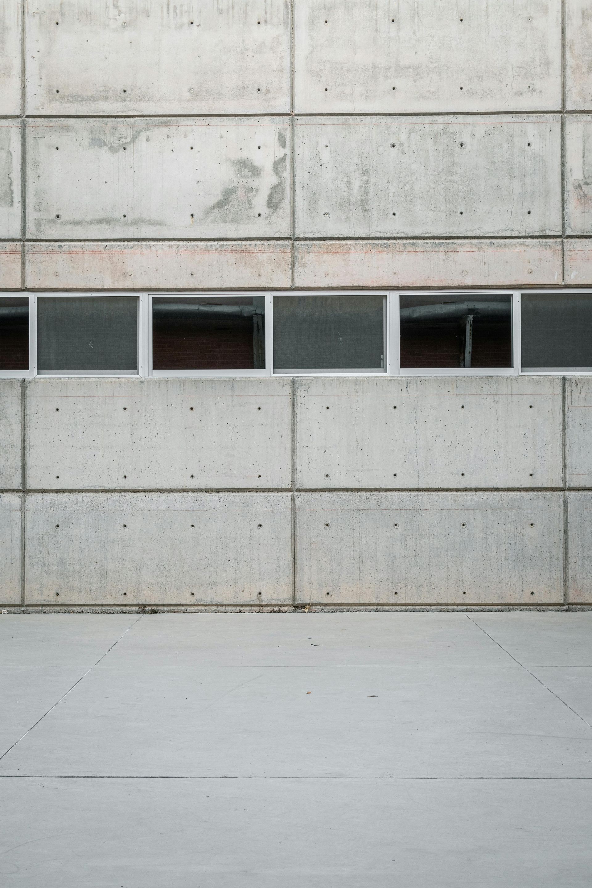 Concrete building wall with a row of small windows above a smooth pavement.